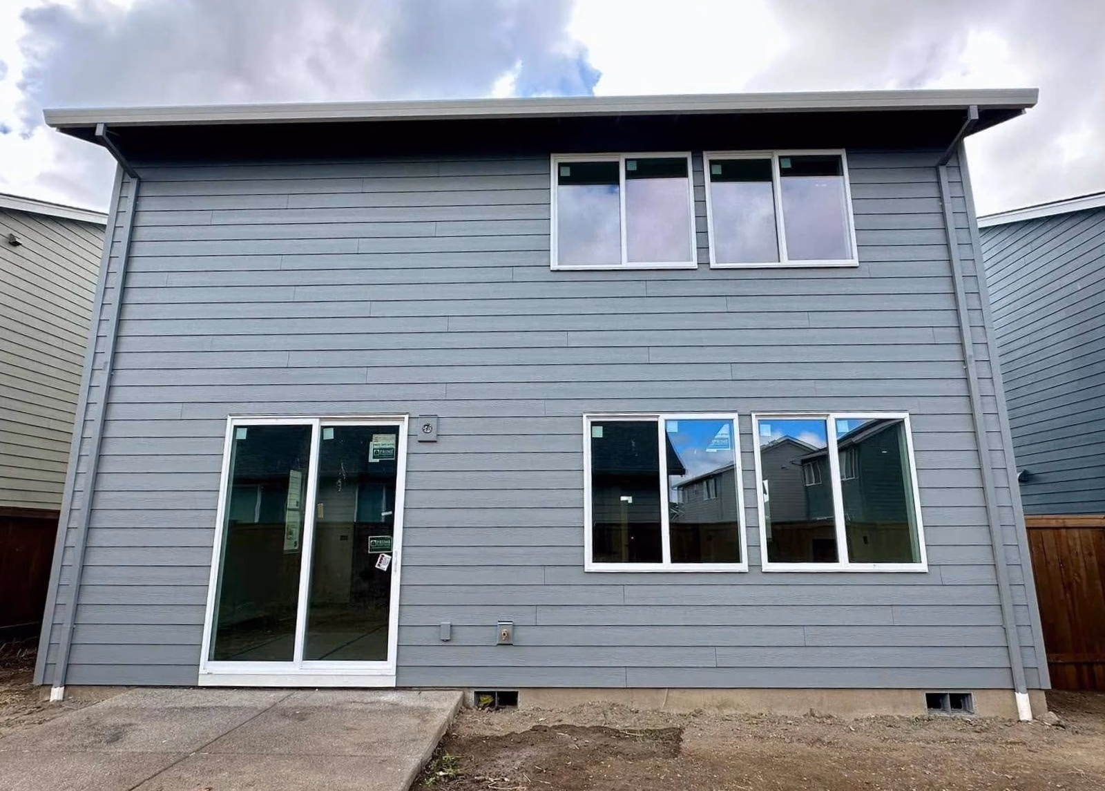 Back of a two-story gray house with three lower windows, one sliding glass door, and two upper windows.