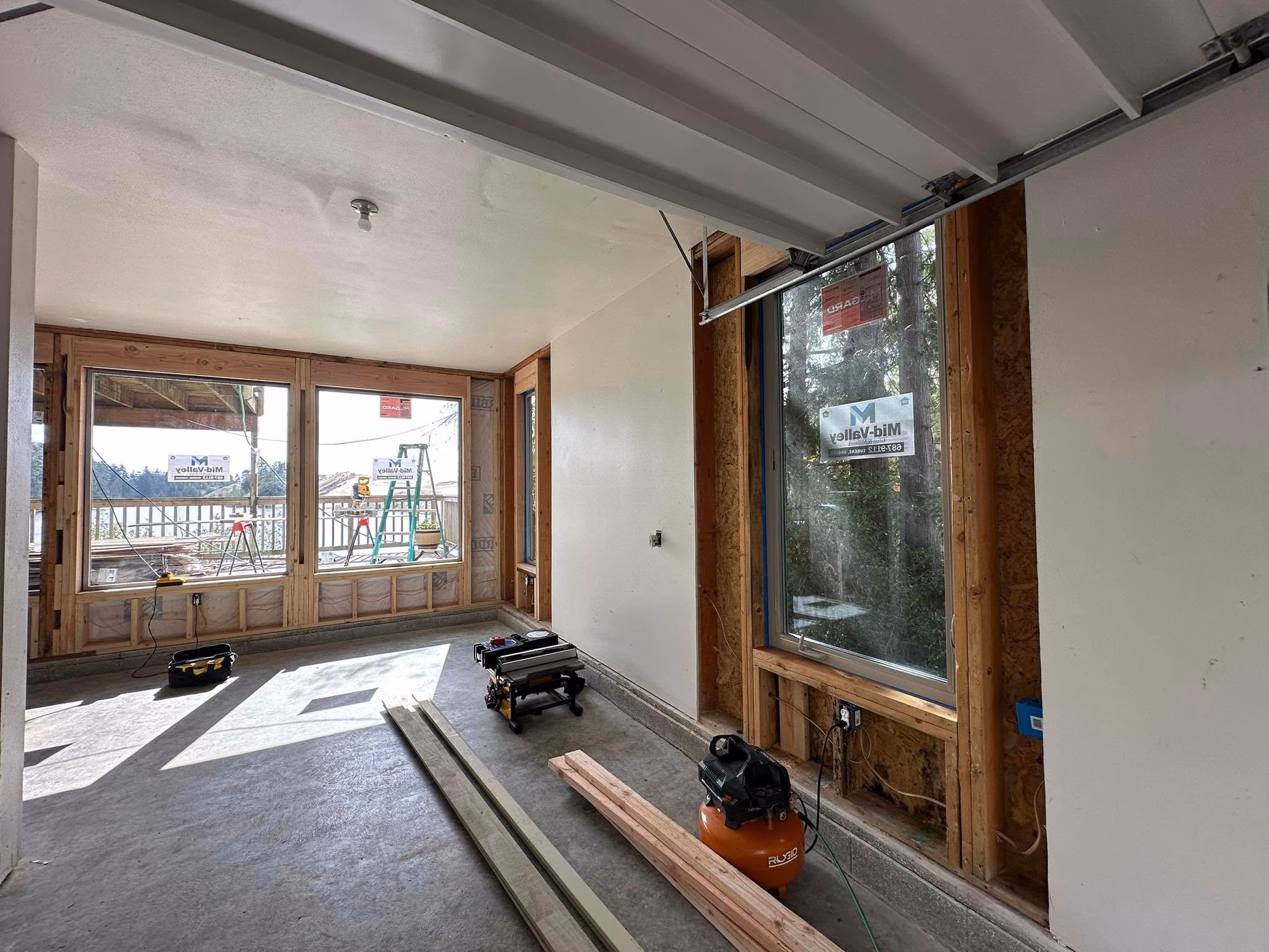 Interior room under construction with large windows, wooden boards, tools, and concrete floor.