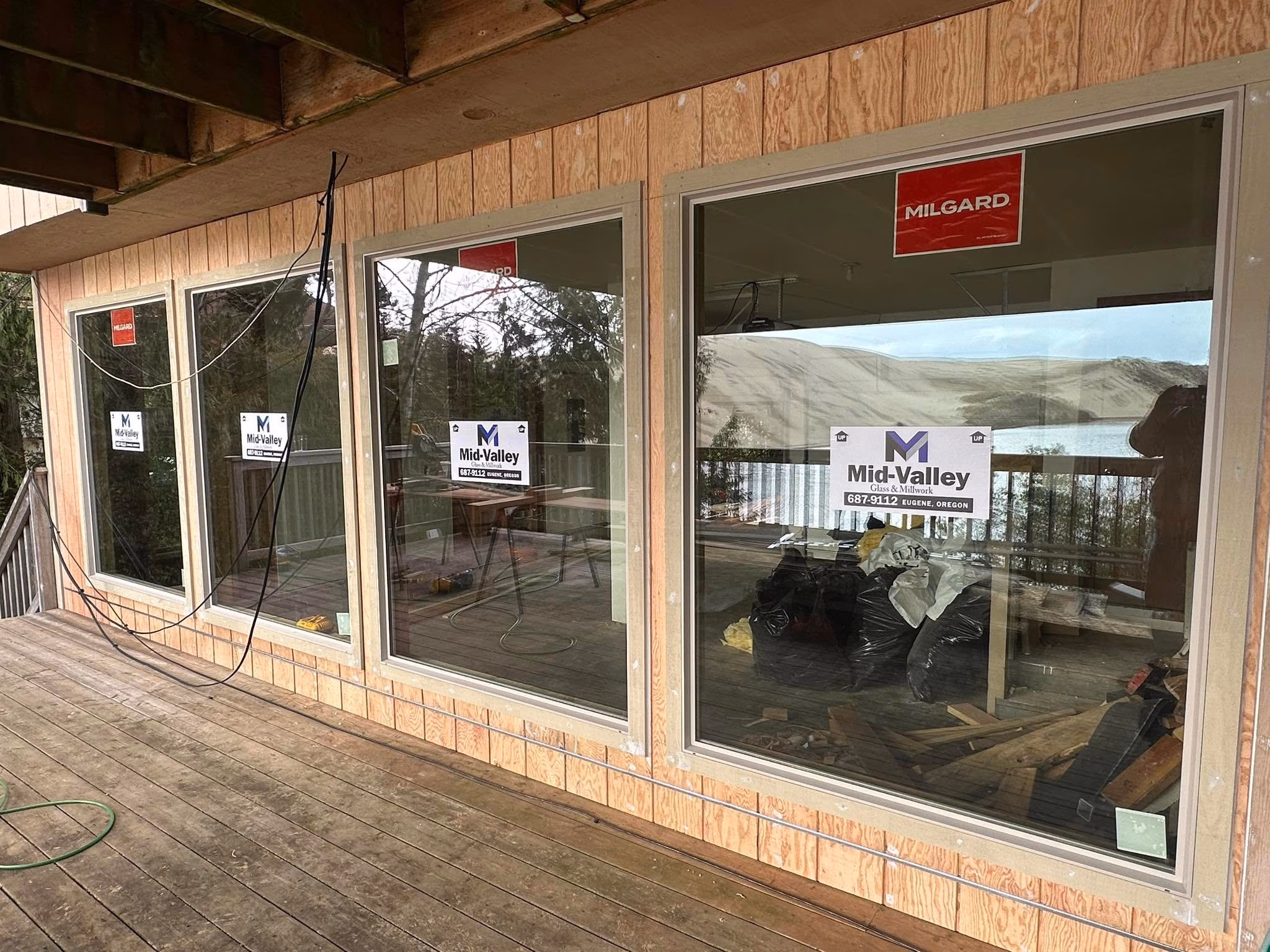 New large windows installed on wood-paneled deck overlooking a lake and hills with tools inside.