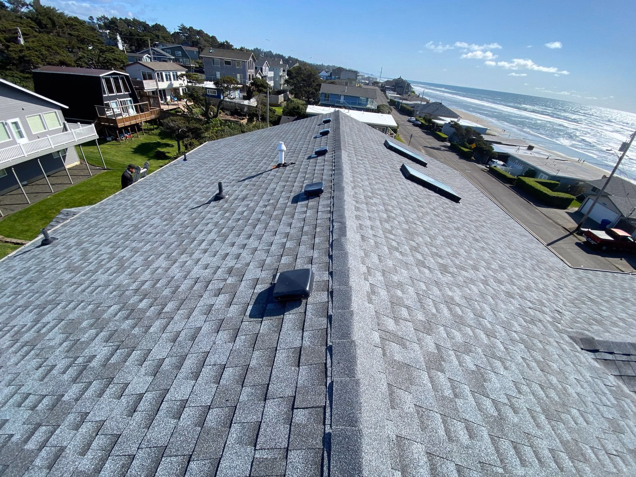 Perspective view of a gray shingle rooftop with skylights by oceanfront houses on a sunny day.
