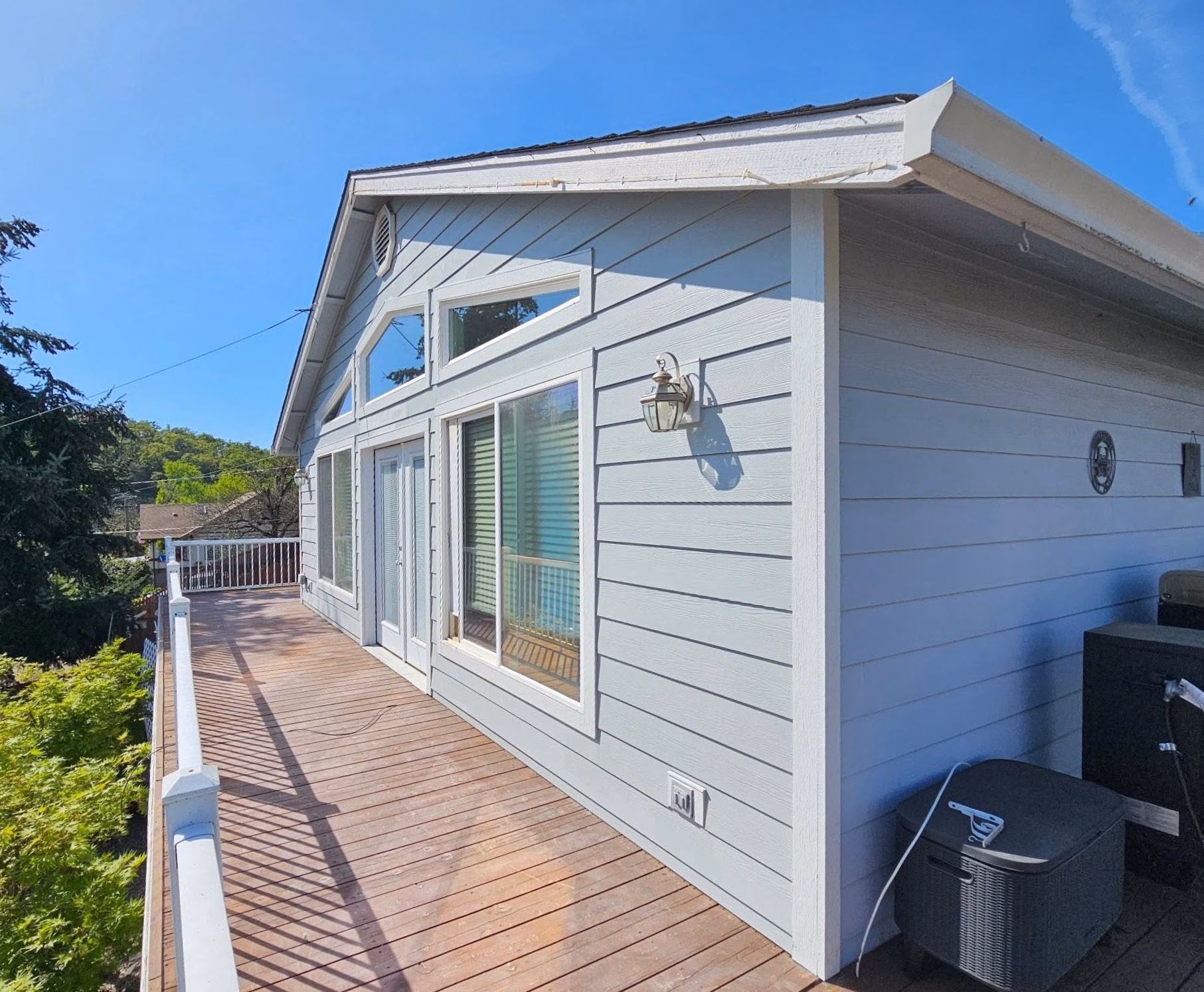 Wooden deck with white railing outside a gray house with multiple windows and glass door.