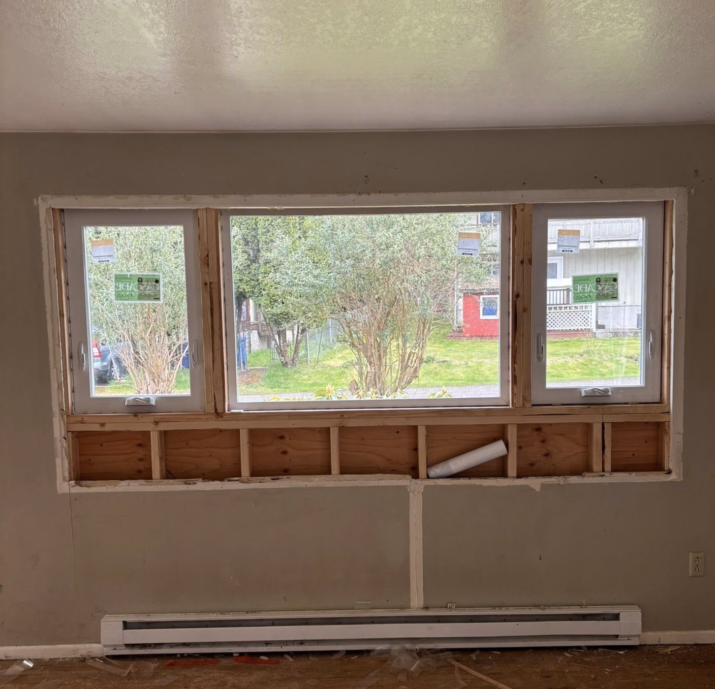 Three-section window partially under construction with exposed wood framing and greenery outside.