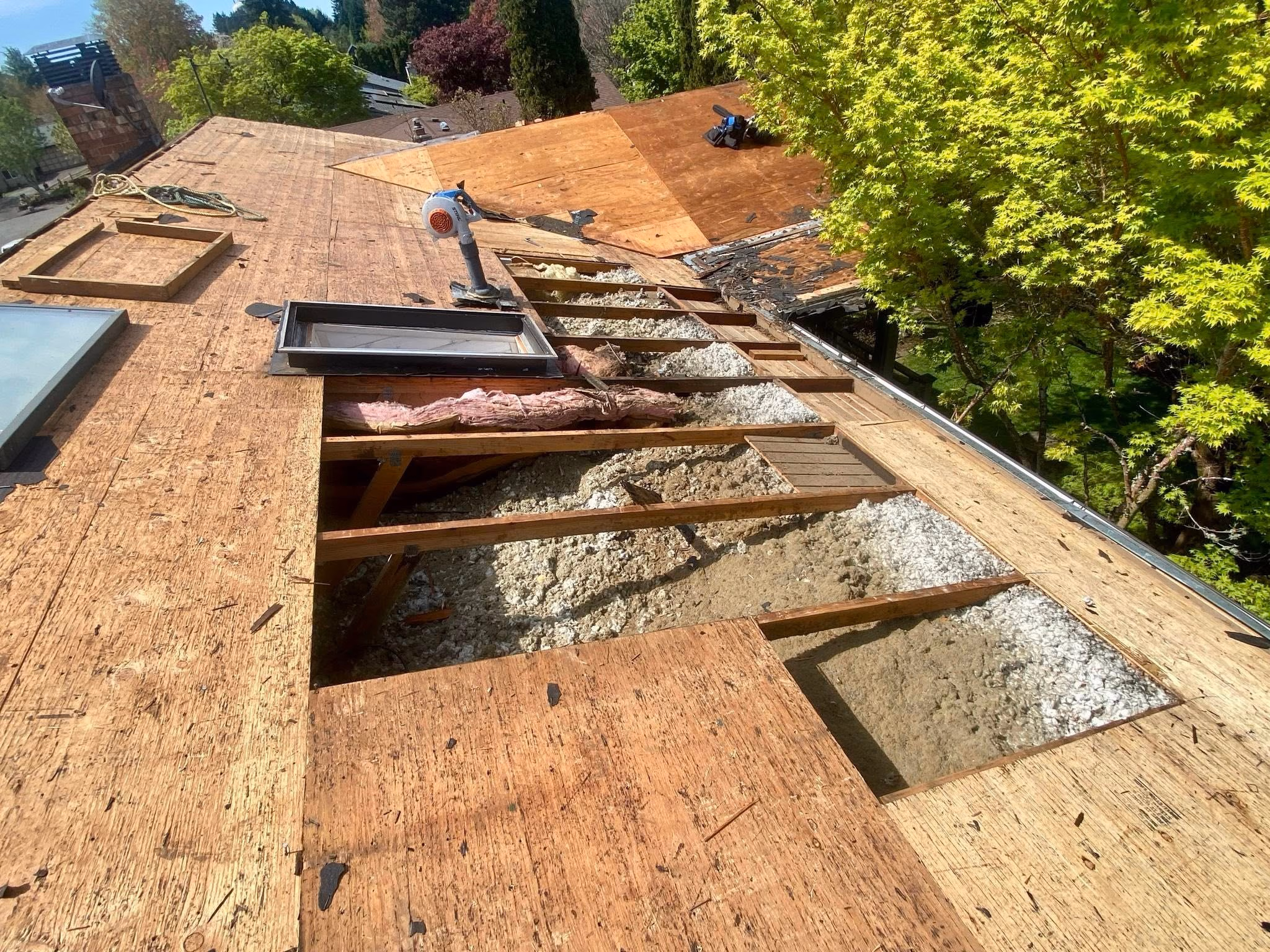 Partially stripped wooden roof with exposed insulation and framing visible under clear sky.