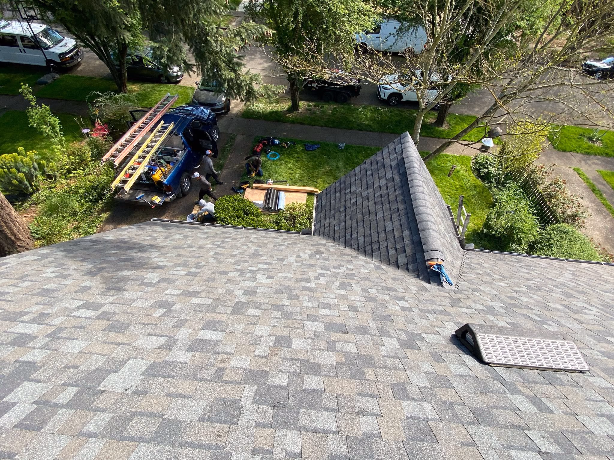 View from rooftop showing workers near a truck with ladders on a green lawn next to the house.