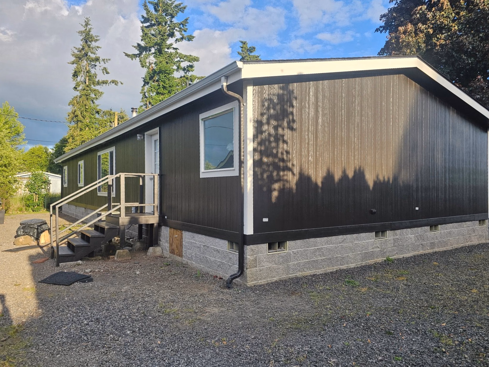 A black and gray mobile home with white-trimmed windows and a wooden staircase entrance.