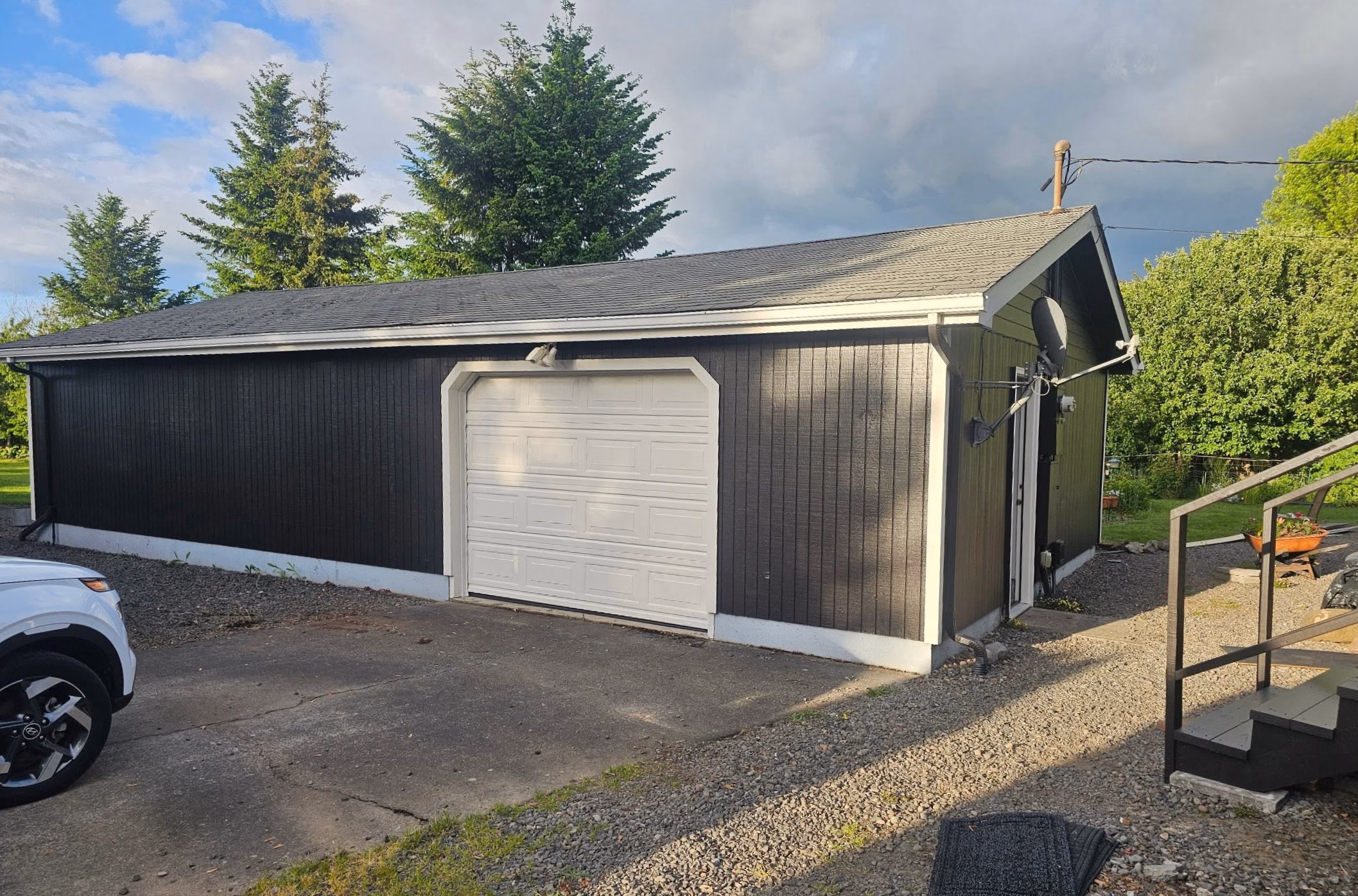 Black garage with white door beside gravel path and white SUV parked on concrete driveway.