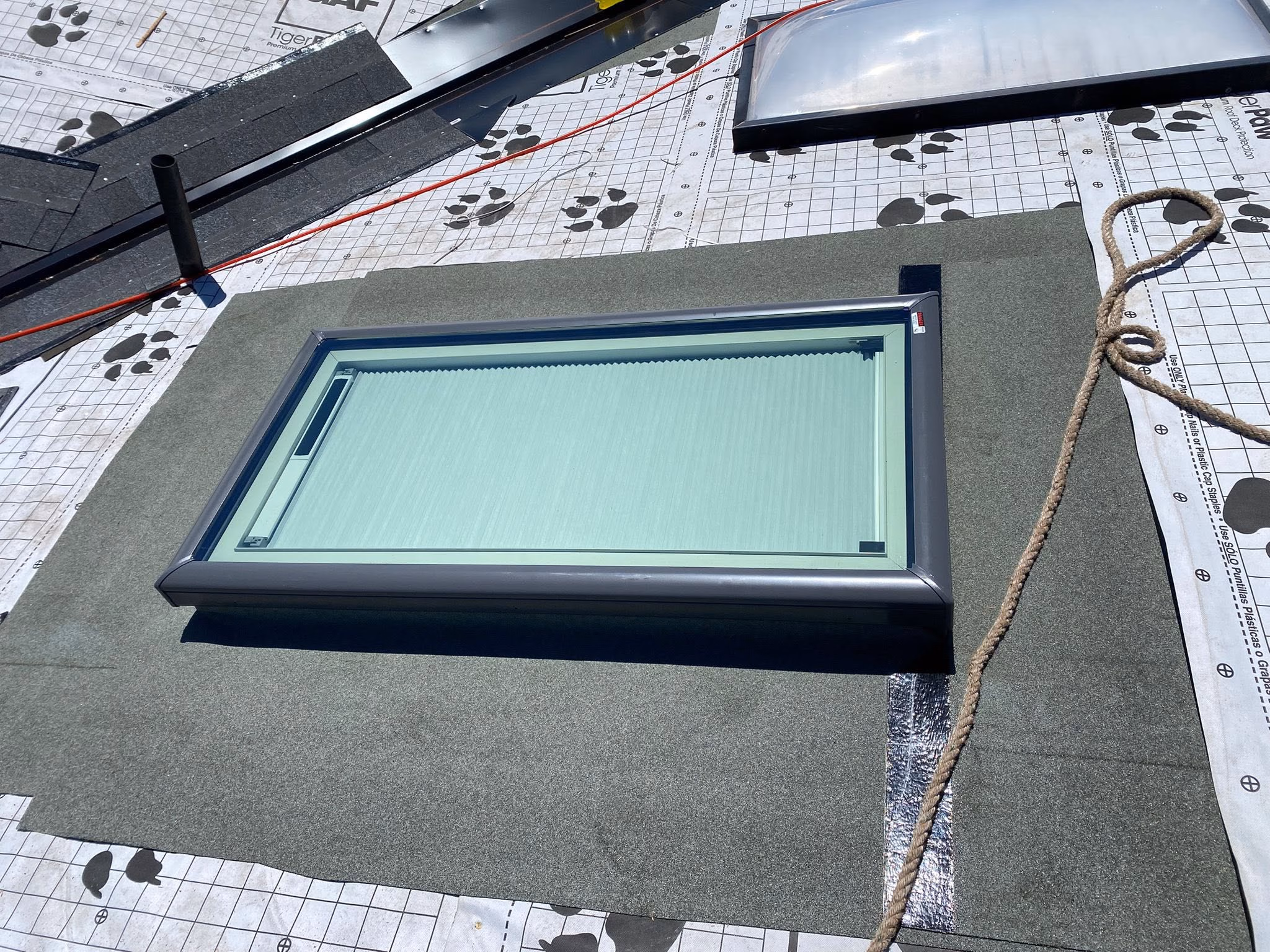 Newly installed rectangular skylight with a closed blind on a roof under construction.