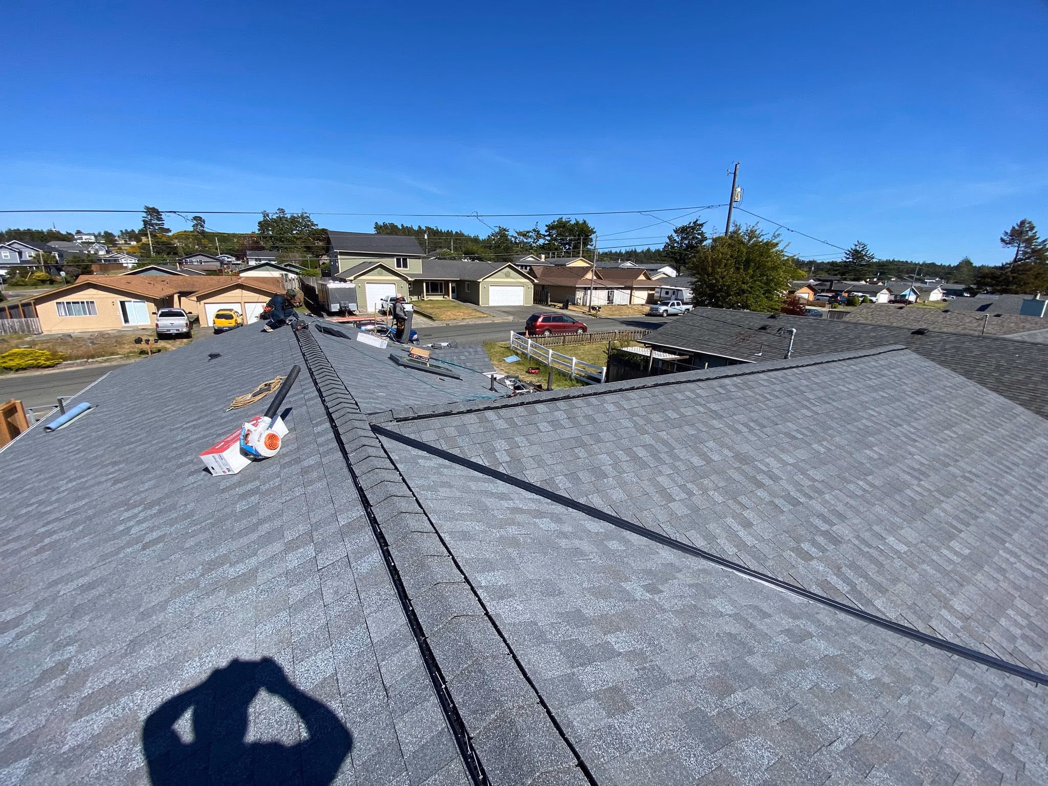 Workers installing new gray asphalt shingles on a residential home roof on a sunny day.