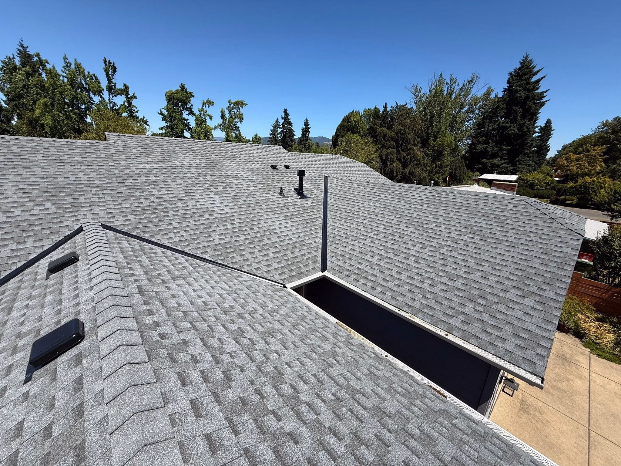 Wide view of a house roof covered with gray asphalt shingles under a clear blue sky.