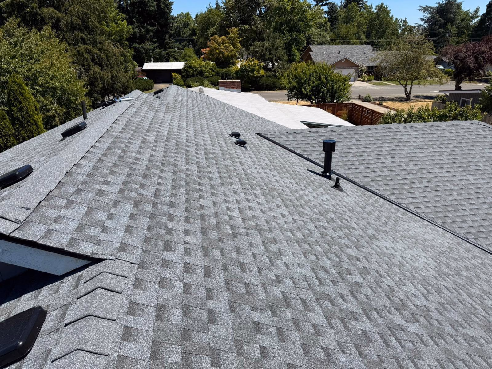 View of gray asphalt shingle roof with vents and a residential neighborhood background.