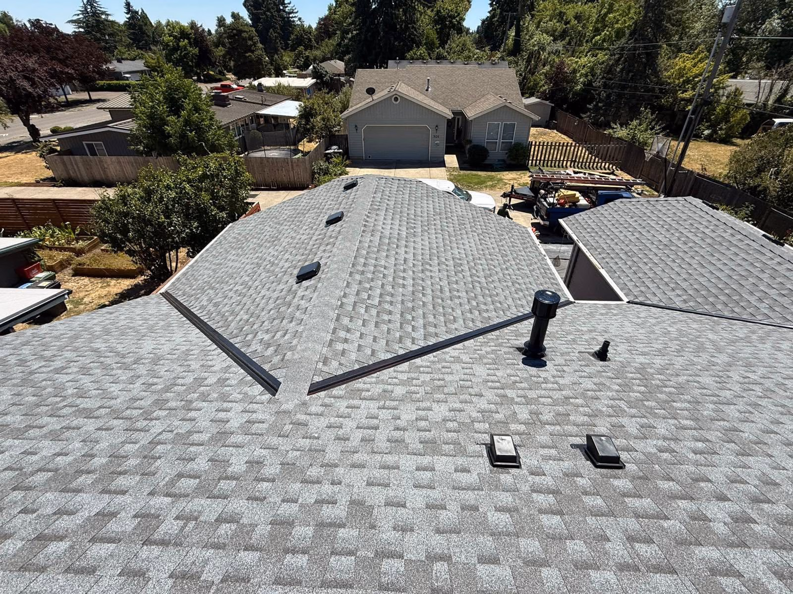 Gray shingled rooftops of houses with vents and chimneys under clear sky.
