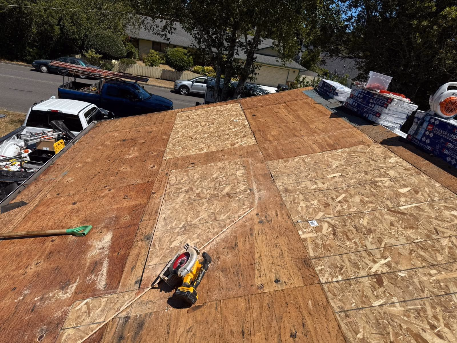 Roof under construction with plywood sheets, tools, and roofing materials stacked nearby.
